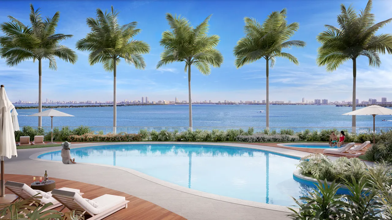 Waterfront pool deck lined with palms, sun loungers and umbrellas facing the water and distant skyline