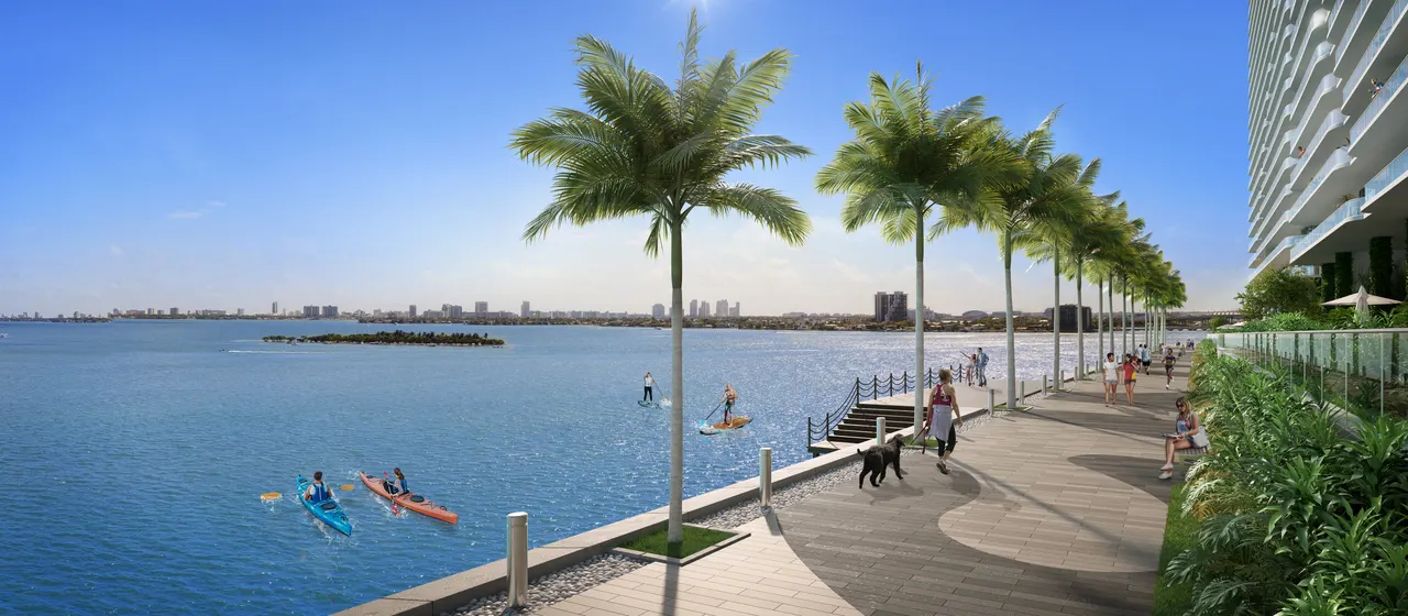 Waterfront baywalk lined with palms beside the tower, with kayakers and paddleboarders on the water