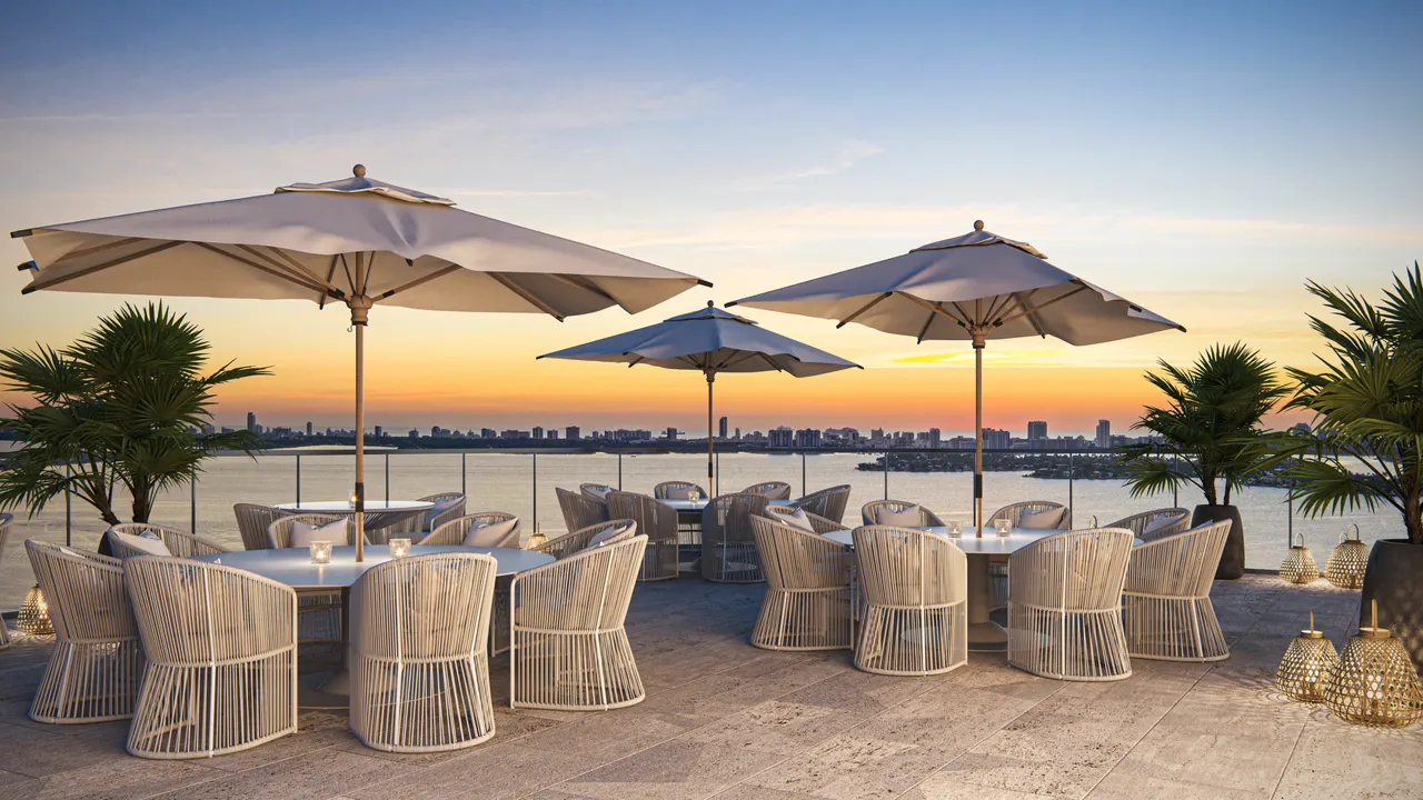 Rooftop terrace with woven dining chairs and umbrellas overlooking the water at sunset