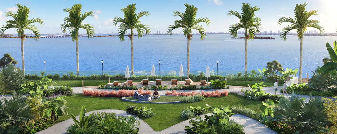 Waterfront lawn with palms, sun loungers and umbrellas overlooking open water and distant skyline