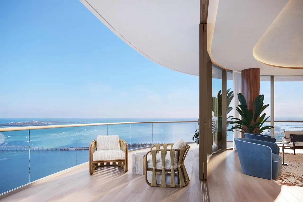 Curved balcony with woven armchairs and glass railing opening to a high-floor water view