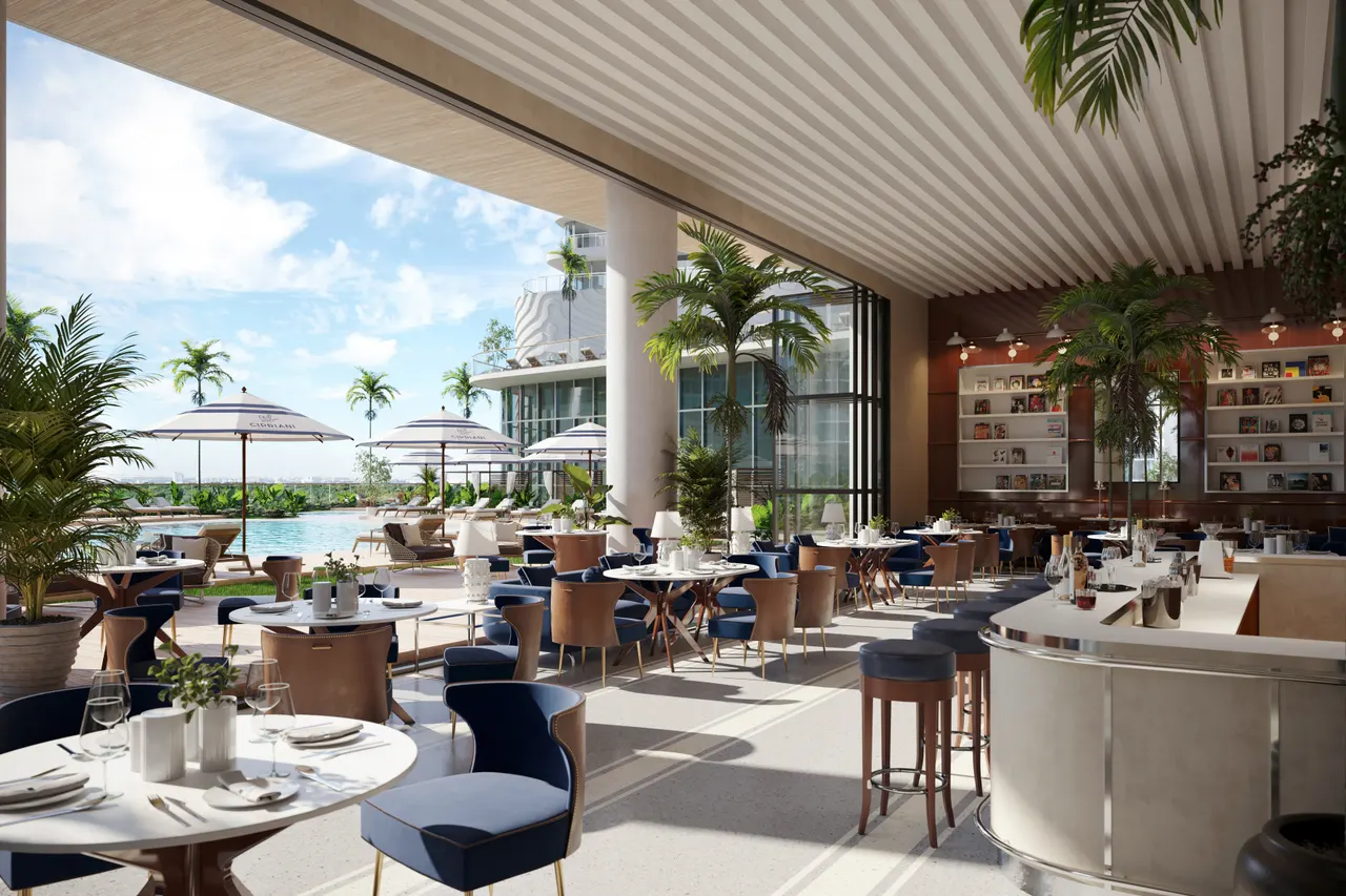 Indoor-outdoor restaurant with navy dining chairs, bar counter and palm-lined pool deck beyond