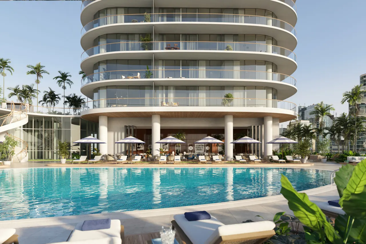 Resort-style pool deck with loungers and blue umbrellas below a curved glass tower at Cipriani Residences