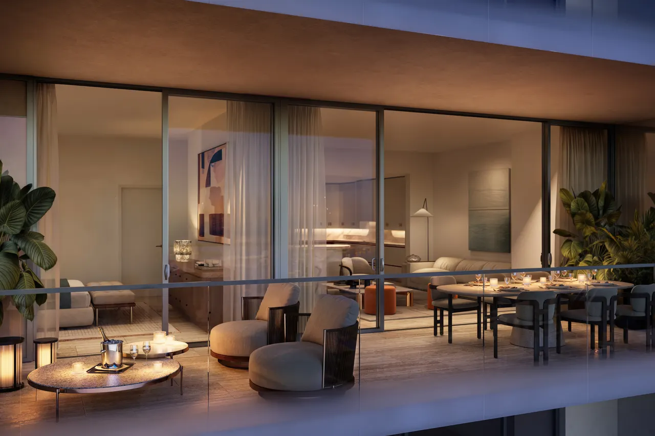 Terrace at dusk with lounge chairs and a dining table beside floor-to-ceiling glass doors