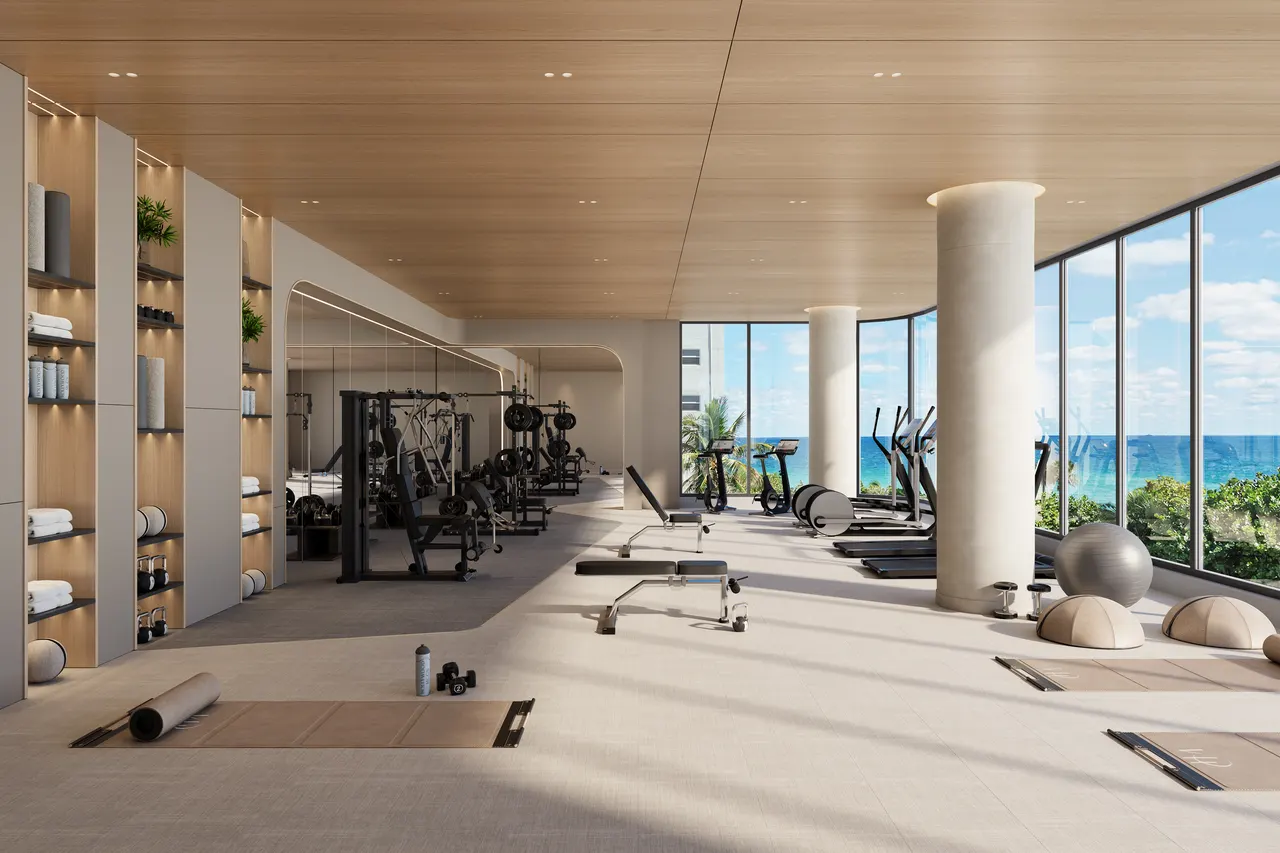 Fitness center with weight machines, treadmills and yoga mats beside floor-to-ceiling windows facing the ocean