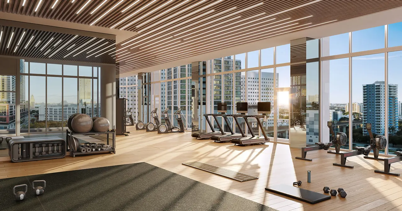 Double-height fitness center with treadmills, free weights and floor-to-ceiling windows over the city