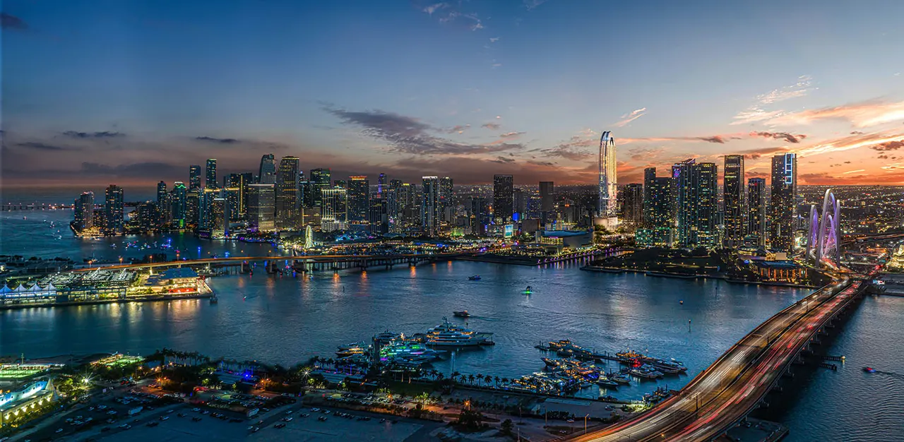 Aerial view of the downtown skyline at dusk with waterfront marinas, bridges and lit city towers