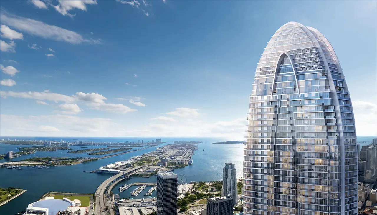 Aerial view of the curved glass tower crown with arched cutout above the waterfront and marina