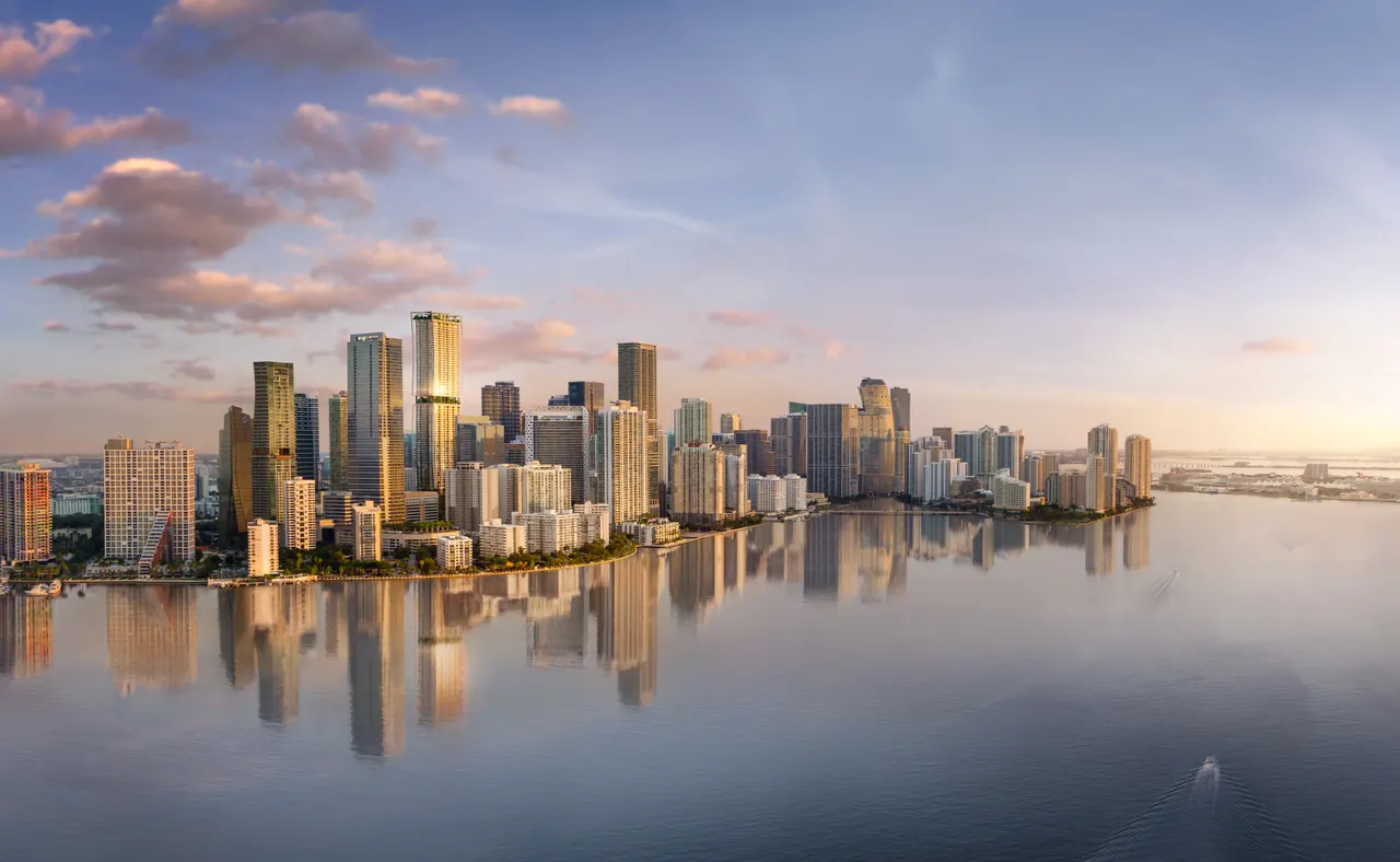 Aerial view of the Brickell skyline at sunset reflected on calm water with a boat passing by