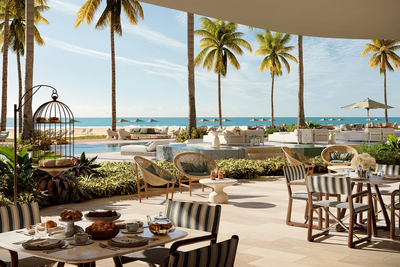 Shaded oceanfront terrace with striped dining chairs, palms and a pool deck beyond