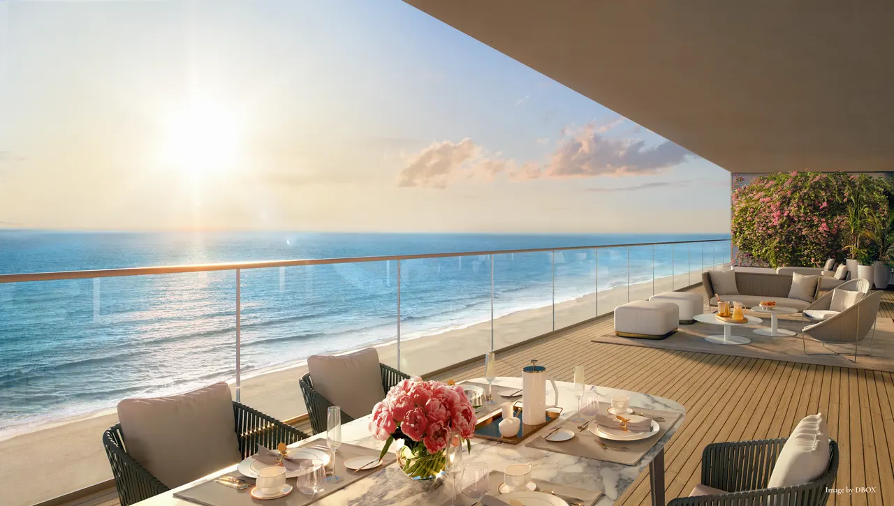 Oceanfront terrace with marble dining table, lounge seating and glass railing over the beach at sunrise