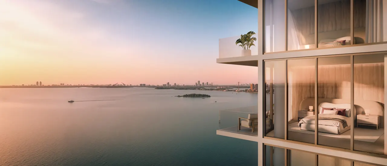 Corner bedroom behind floor-to-ceiling glass with a terrace overlooking the water at sunset
