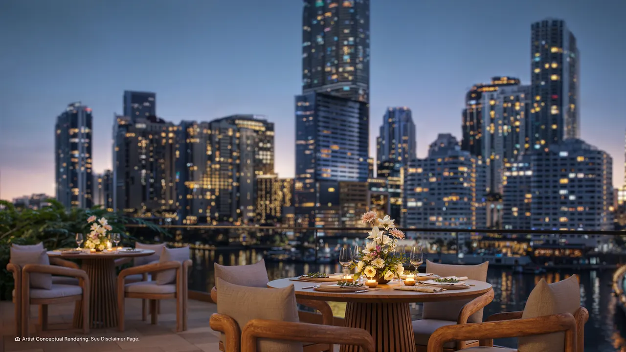 Outdoor dining terrace with set tables facing the illuminated city skyline across the water at dusk
