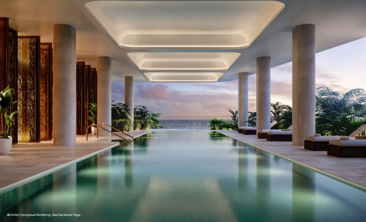Covered lap pool framed by stone columns and backlit ceiling panels, opening to a water view at dusk