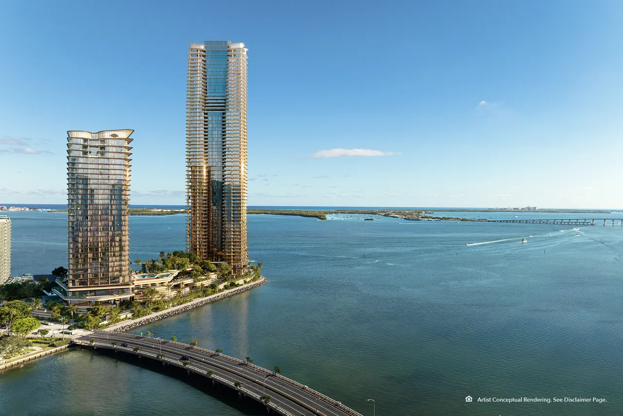 Aerial view of two waterfront glass towers on a point, with a causeway bridge and open bay beyond
