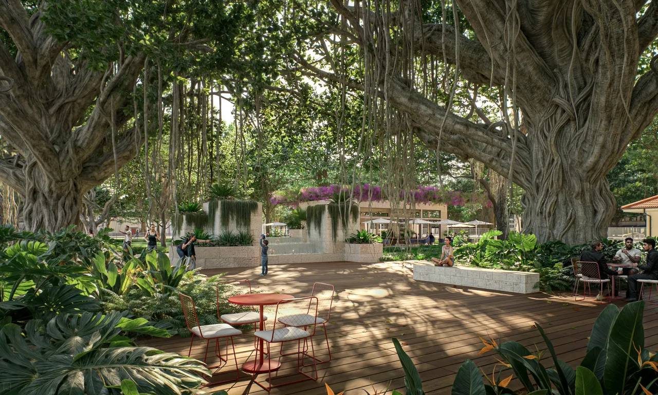 Shaded wood deck plaza beneath banyan trees with cafe tables, planters and a water feature
