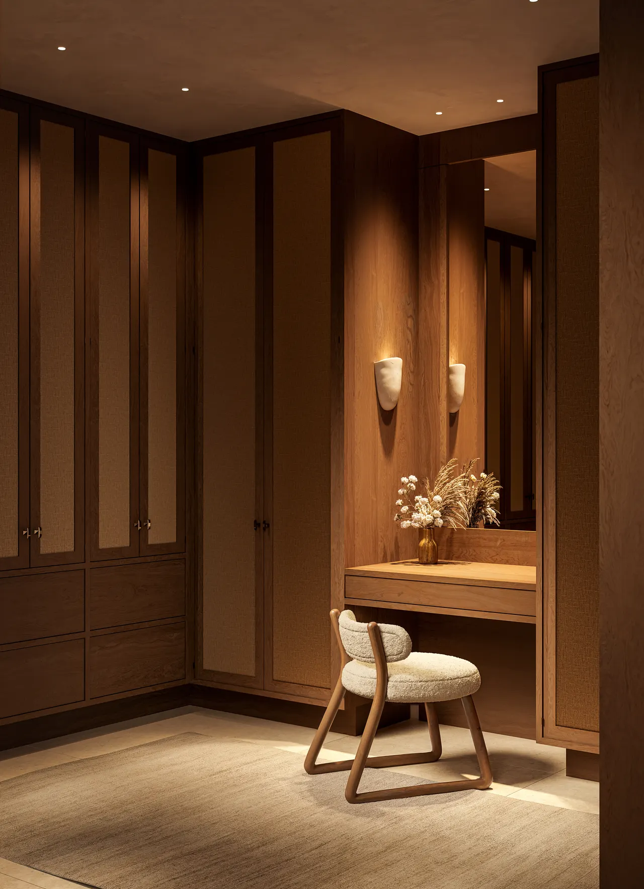 Walk-in closet in warm wood with built-in vanity, mirror, sconces and upholstered chair